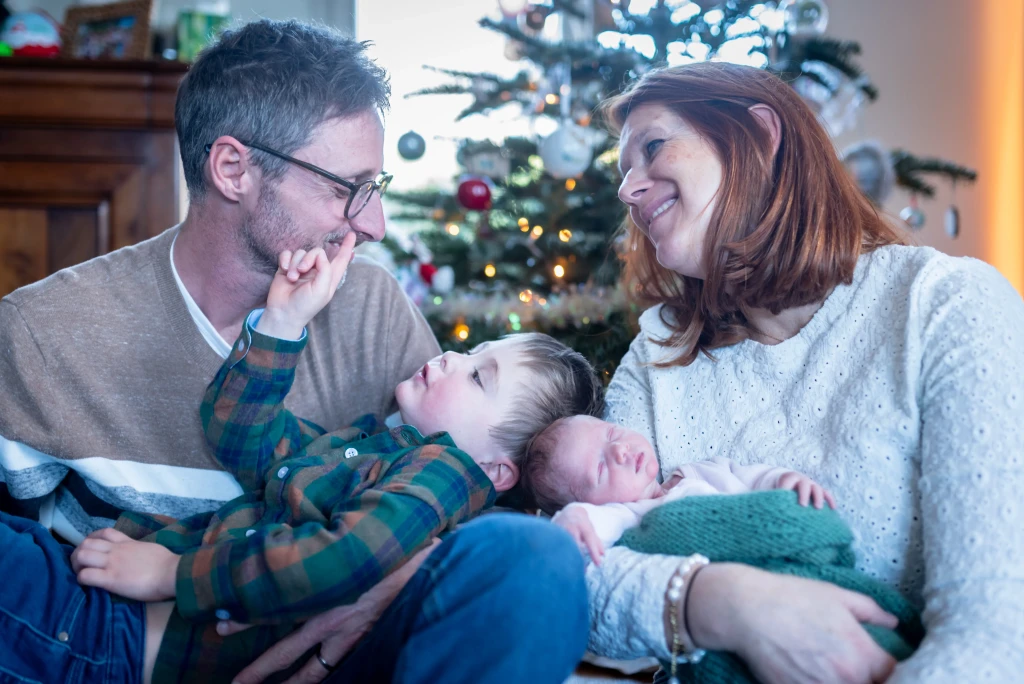 Portrait d'une famille de 4 personnes devant un sapin de Noël. On voit les parents avec leur fils aîné et leur bébé nouveau-né